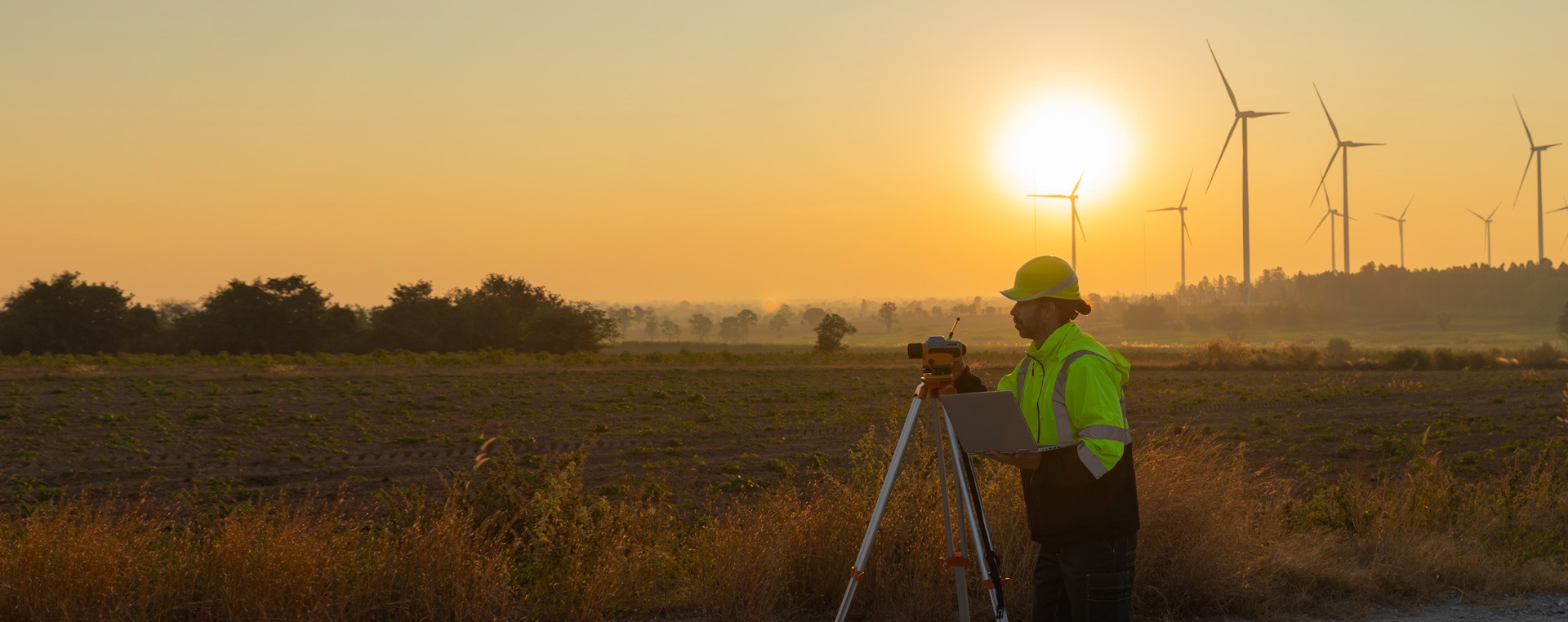 Engineer surveying land with windmills in the background